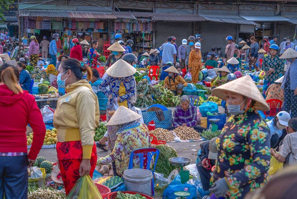 Busy morning scene at Vi Thanh squat-down market in Hau Giang with locals shopping and vendors sitting on low stools