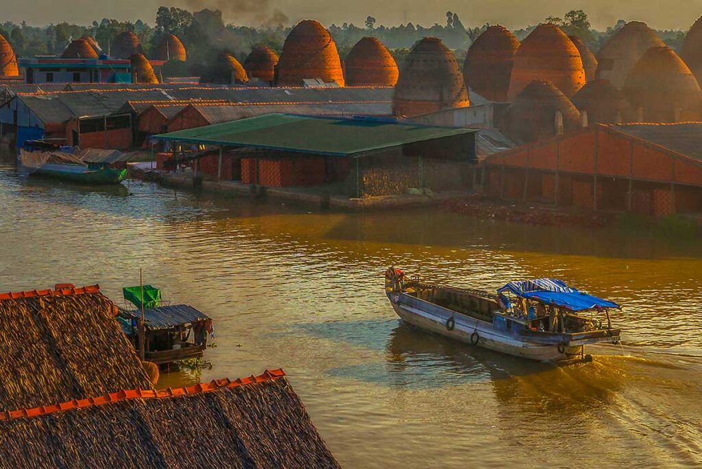 Boats passing Mang Thit brick kilns on the Co Chien River at sunset in Vinh Long