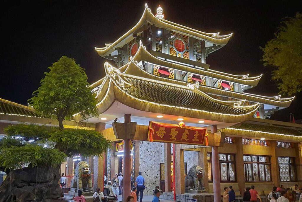 Ba Chua Xu Temple illuminated at night in Chau Doc, with glowing rooflines and worshippers entering the main hall.