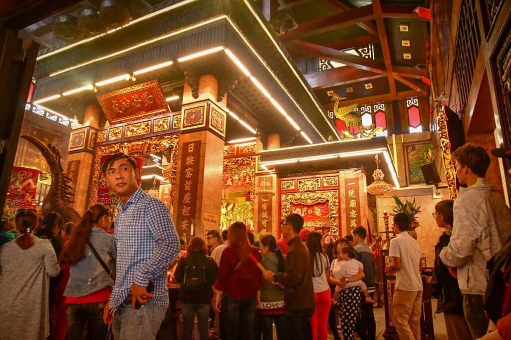 Crowds gathered in the richly decorated main hall of Ba Chua Xu Temple in Chau Doc, with golden carvings and red altars.