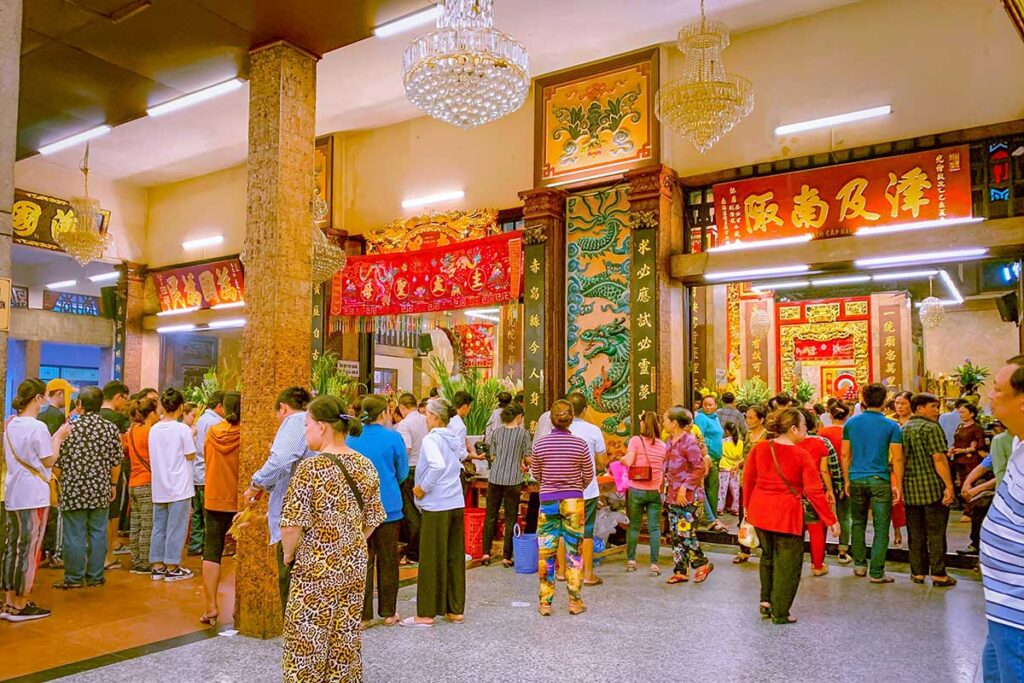 Worshippers lining up inside Ba Chua Xu Temple, Chau Doc, to make offerings beneath colorful banners and ornate carvings.