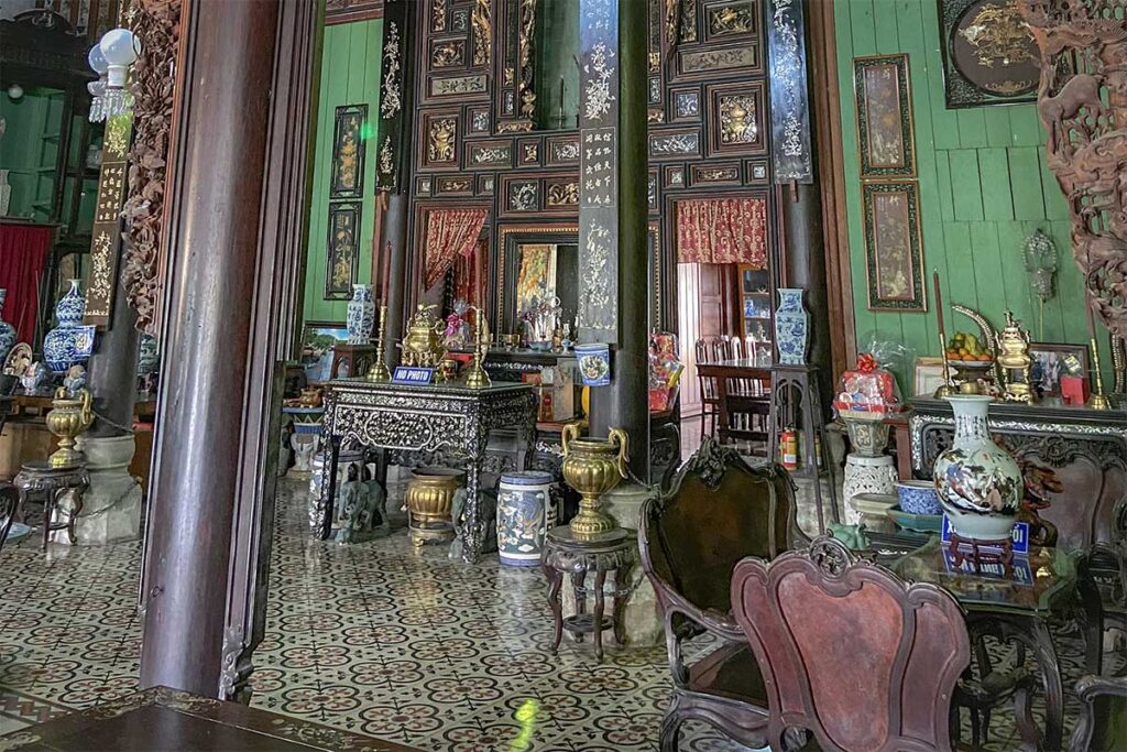 Traditional altar room with antique furniture, wooden columns, and French floor tiles inside Binh Thuy Ancient House.