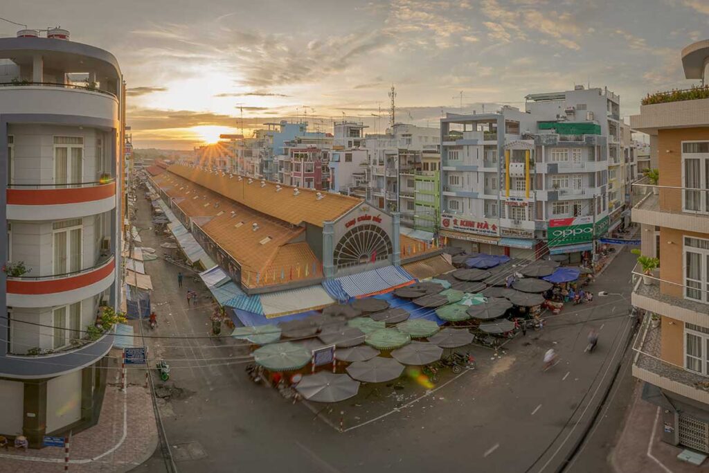 Chau Doc Market in An Giang at sunrise, with street stalls and the central market hall surrounded by city buildings.