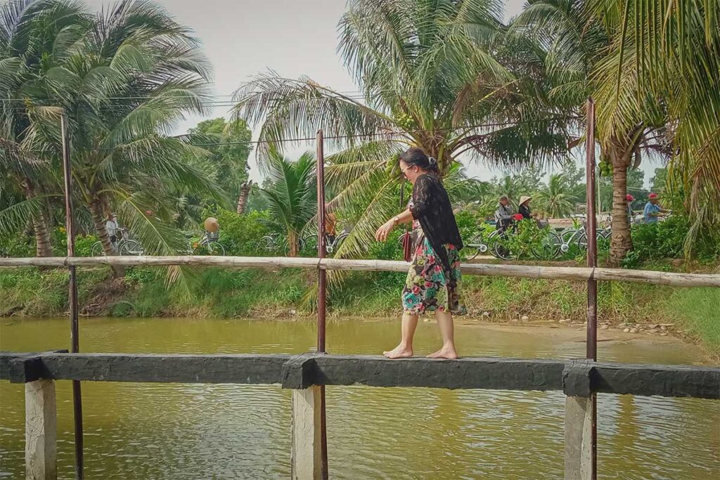 Local woman crossing a narrow bamboo bridge over a pond on Con Chim Island, Tra Vinh, a popular folk game for visitors