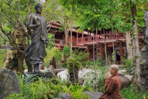 A Buddhist monk in prayer before a standing Buddha statue in the garden courtyard of Huyen Khong Son Thuong Pagoda, Hue.