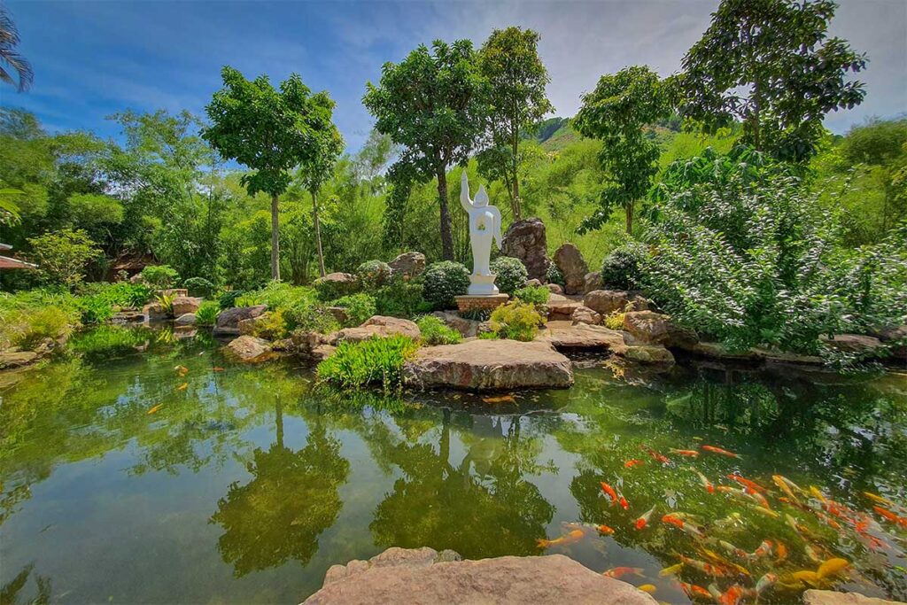 Ornamental pond with koi fish and a white Buddha statue in the gardens of Huyen Khong Son Thuong Pagoda, a peaceful hidden gem in Hue.