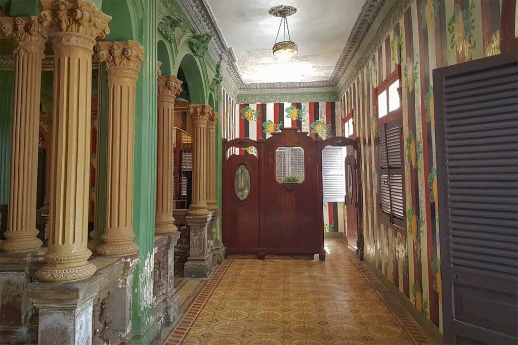 Hallway inside Huynh Ky Ancient House with decorative columns, patterned floor tiles, and vintage wooden partition.