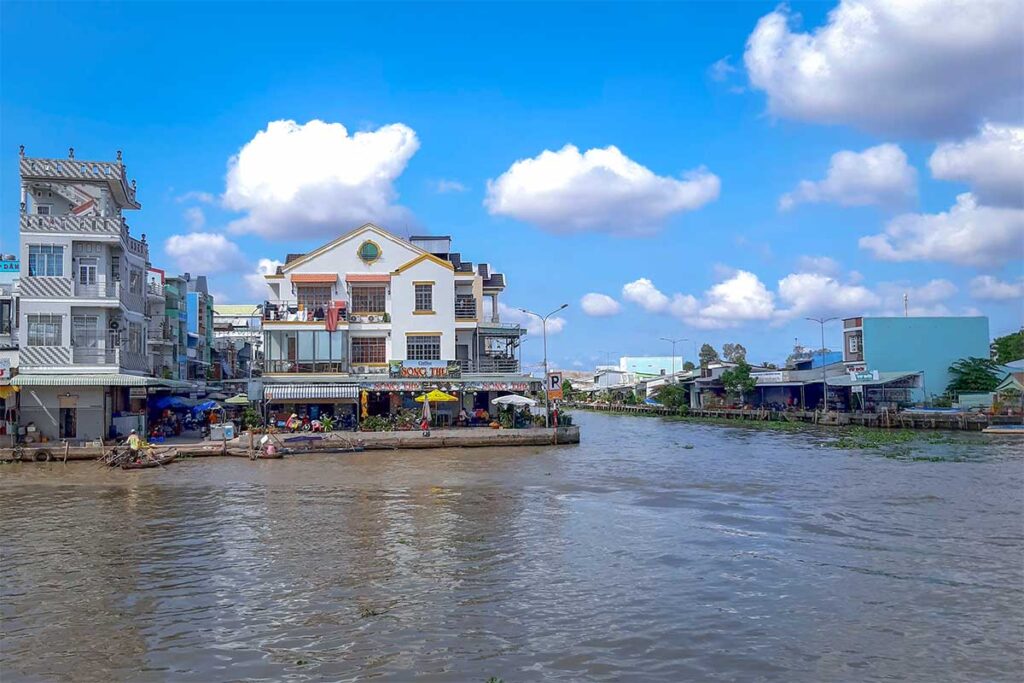 Street and houses facing the canal in Nga Nam town under a bright blue sky.