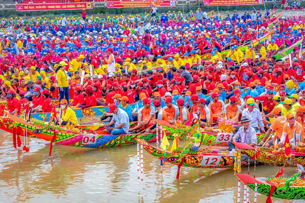 Mass gathering of Khmer rowing teams in colorful uniforms preparing their decorated longboats at the Ghe Ngo Boat Race Festival in Soc Trang, Vietnam.
