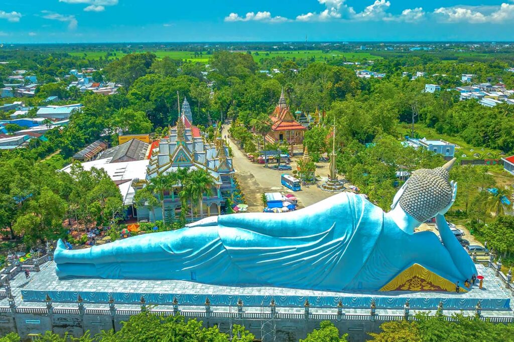 Daytime aerial view of the massive reclining Buddha statue at Som Rong Pagoda, with Khmer temple roofs and Soc Trang city in the background