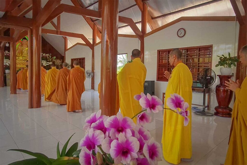 Monks in yellow robes chanting inside the main hall at Van Phuoc Pagoda, Ben Tre