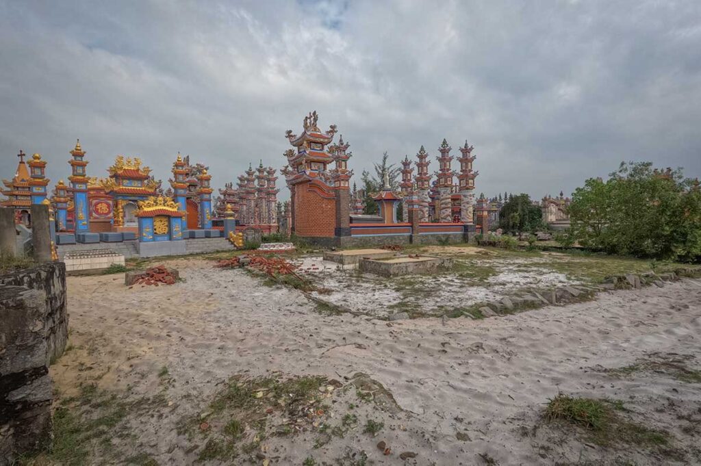 View across the vast City of Ghosts near Hue, with rows of intricately built tombs in red, gold, and blue standing on the white coastal sand of An Bang village.