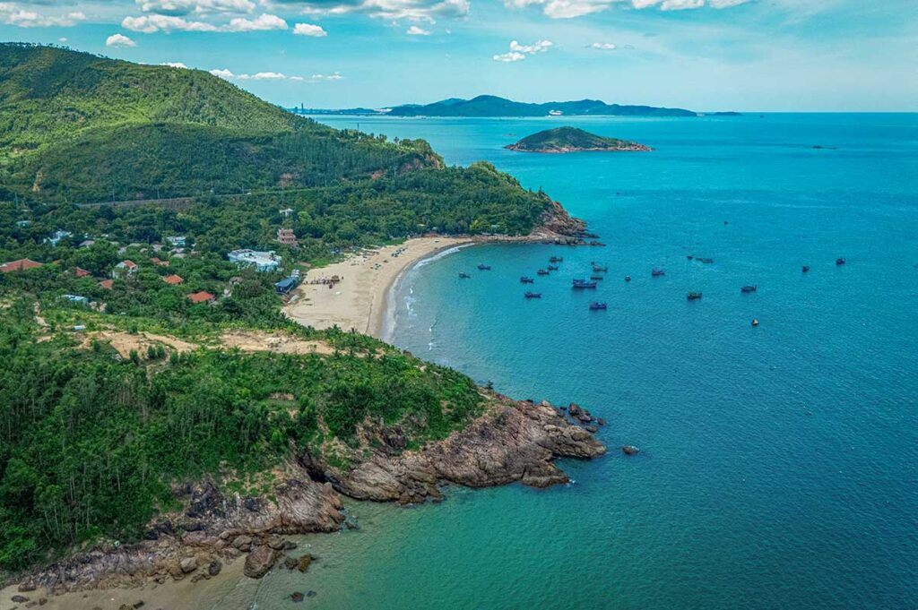 Aerial view of Bai Bang Beach, Quy Nhon: small sandy cove, turquoise water, fishing boats, forested headlands.