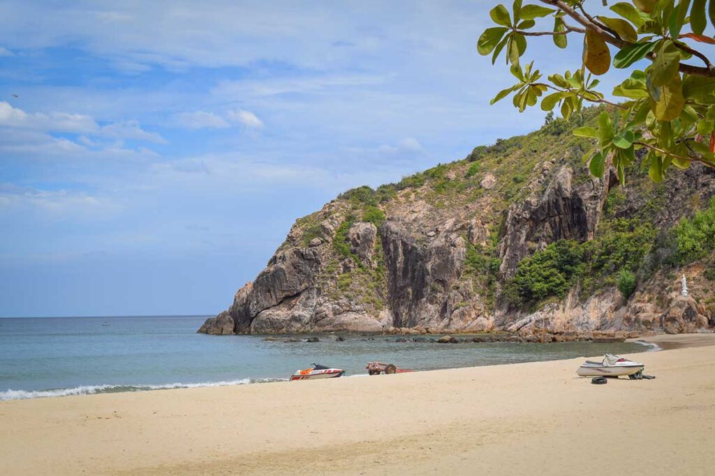 Bai Bau Beach, Quy Nhon: quiet golden sand under a rocky headland with gentle waves, peaceful swim spot.