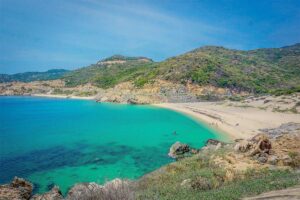Aerial-style view of Bai Mon Beach in Phu Yen, Vietnam, with turquoise water, golden sand, and rugged green hills surrounding the bay.