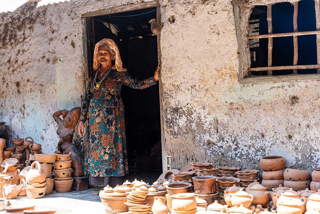 Cham woman standing at the doorway of her pottery workshop, surrounded by handmade terracotta jars and cooking pots in Bau Truc Village.