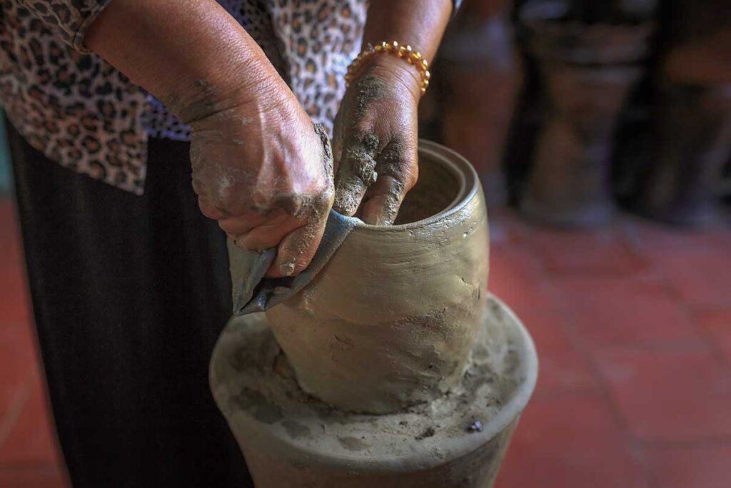 Hands of a Cham potter smoothing a clay vase during the finishing process in Bau Truc Pottery Village.