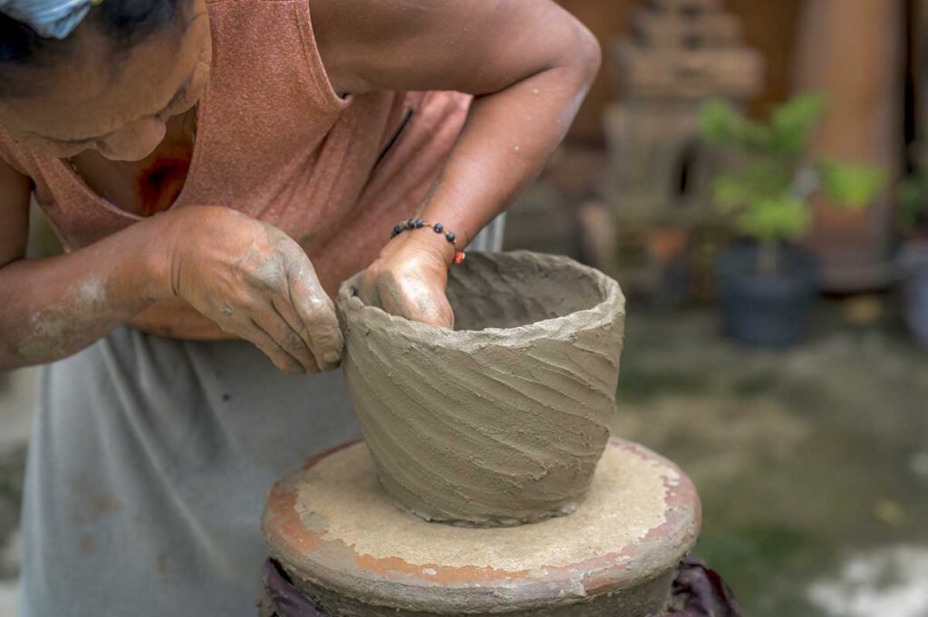 Close-up of Cham artisan crafting a clay pot by hand at Bau Truc Pottery Village, showing traditional techniques.