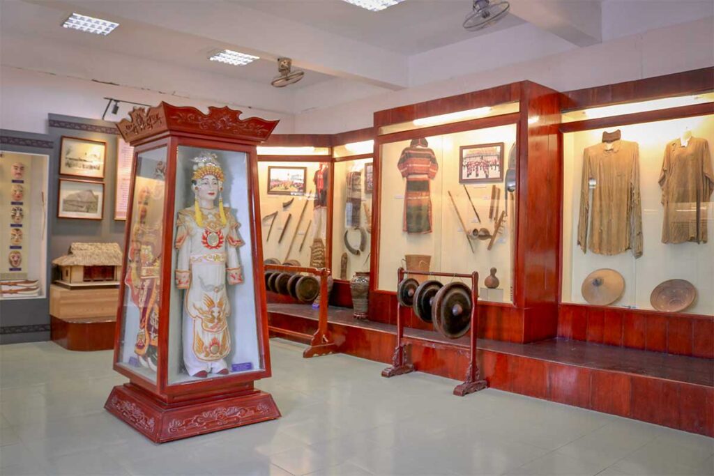 Traditional culture exhibits at Binh Dinh Museum in Quy Nhon, featuring ethnic costumes, musical gongs, and ceremonial statue.