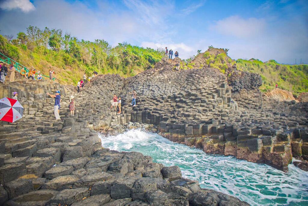 Tourists walking and taking photos on the basalt rock formations of Da Dia Reef, the Sea Cliff of Stone Plates in Phu Yen, Vietnam.