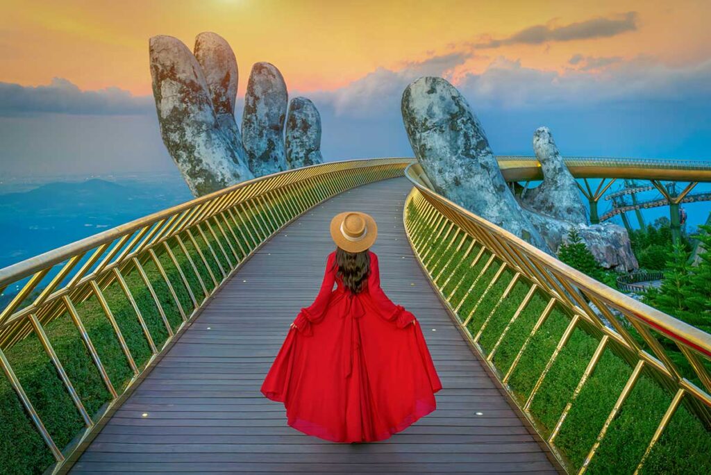 Da Nang tours – Local Vietnam | traveler in red dress walking on the Golden Bridge at Ba Na Hills during sunrise