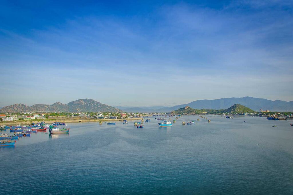 Wide view of Dam Nai Lagoon behind Ninh Chu Beach, dotted with fishing boats and surrounded by Ninh Thuan mountains