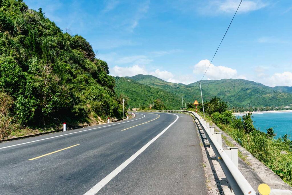 Deo Ca Pass road along the coast – Smooth asphalt curves of Deo Ca Pass road hugging the mountainside with views over the turquoise coastline.