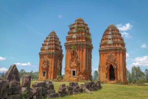 The three Duong Long Cham Towers rising above scattered sandstone carvings in the foreground, a vivid example of Cham architecture in Binh Dinh.