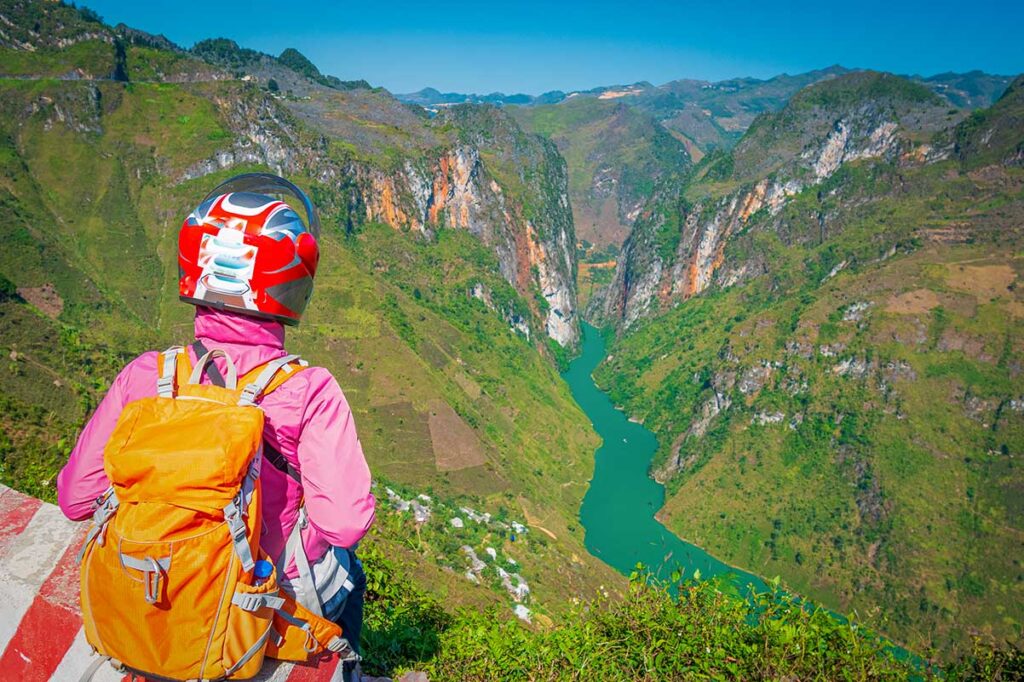 Ha Giang Loop motorbike tour – Local Vietnam | traveler with helmet overlooking deep canyon and river valley in Ha Giang