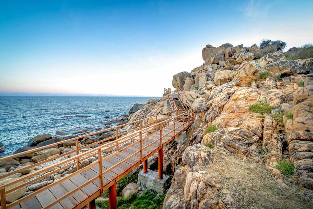 Hang Rai boardwalk along rocky coastline in Nui Chua National Park, Ninh Thuan, Vietnam – wooden path leading over dramatic stone formations by the sea.