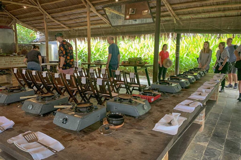Cooking class station with gas stoves and utensils set up under a thatched roof pavilion in Hoi An.