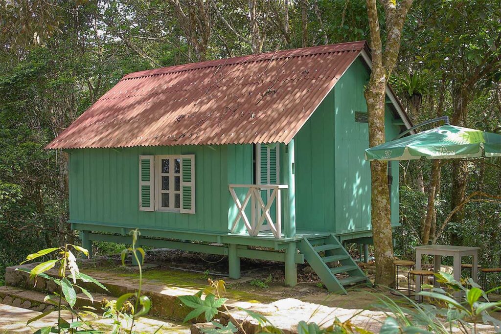 Rustic green wooden bungalow hidden among trees at Hon Ba Nature Reserve.