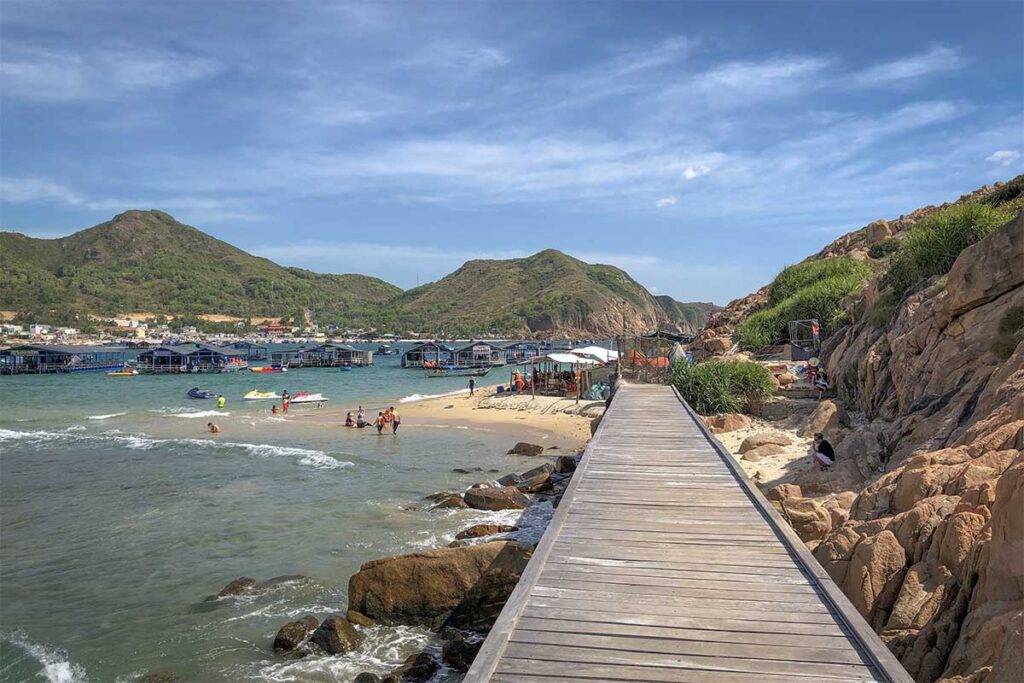 Wooden boardwalk at Hon Kho Island – A narrow walkway built along the rocks, leading to sandy coves and views back towards Nhon Hai Peninsula.