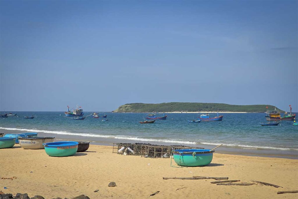Round coracle boats on Long Thuy Beach – Basket boats and fishing nets scattered on golden sand with Hon Chua island visible in the distance.