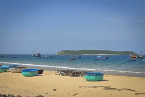 Round coracle boats on Long Thuy Beach – Basket boats and fishing nets scattered on golden sand with Hon Chua island visible in the distance.