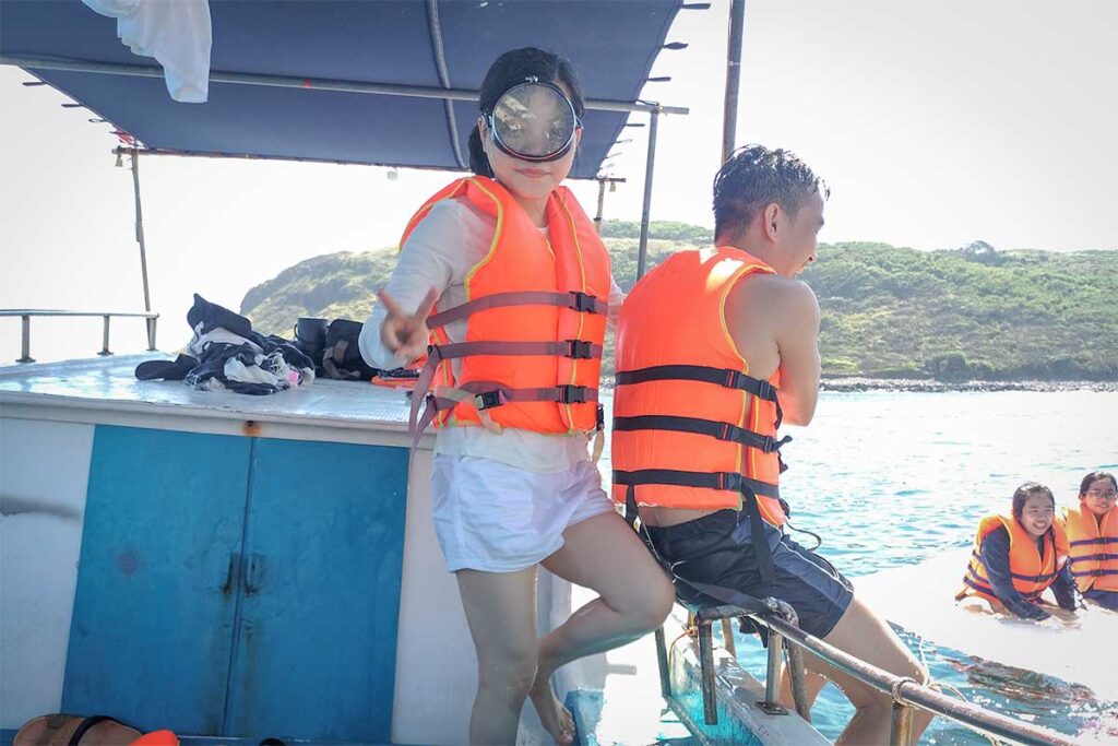 Tourists on a local boat tour from Long Thuy Beach wearing life vests, preparing to snorkel near the offshore islets of Phu Yen.