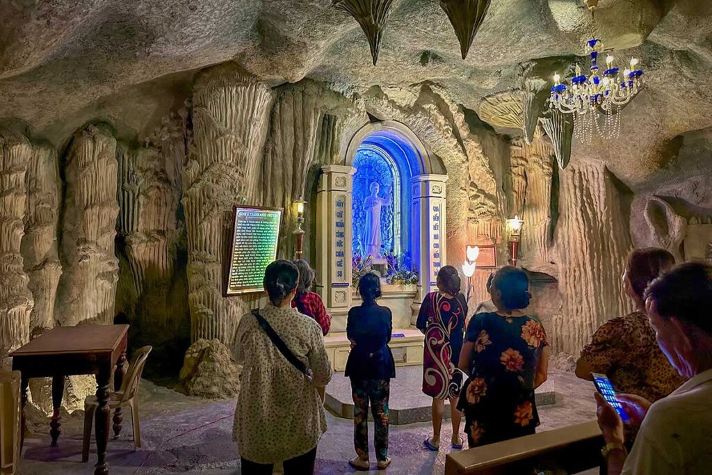Pilgrims praying inside the cave chapel at Mang Lang Church, lit with chandeliers and a glowing statue niche.