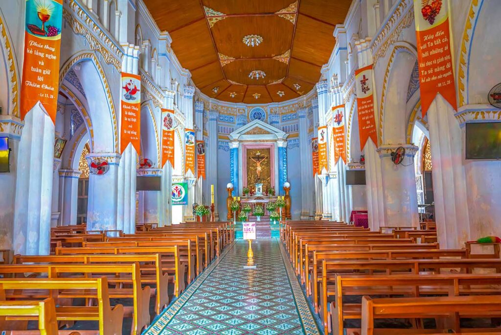 Inside Mang Lang Church, with Gothic arches, wooden ceiling panels, tiled floor, and decorated altar.