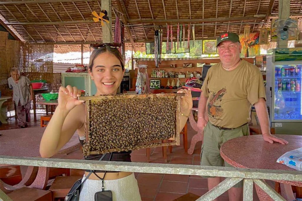 Teenager visiting a honey farm in the Mekong Delta, holding a frame full of bees during a family-friendly workshop experience.
