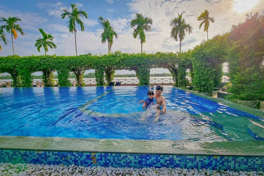 Father playing with his child in a riverside swimming pool at Mekong Lodge in the Mekong Delta, a relaxing option for families with kids.