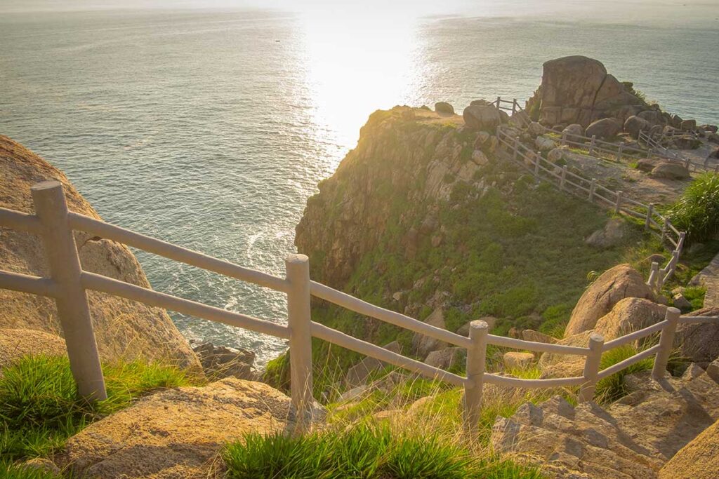 Cliffside pathway at Mui Dien Cape in Phu Yen overlooking the East Sea during golden sunset light.
