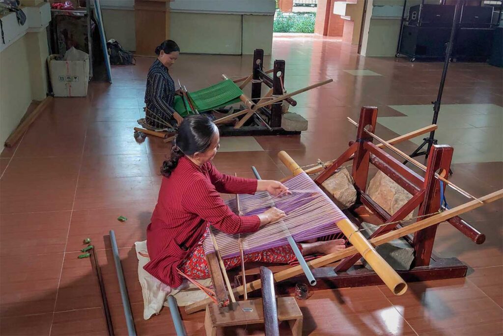 Cham women weaving brocade fabric by hand on traditional looms at My Nghiep Brocade Weaving Village in Ninh Thuan, Vietnam.
