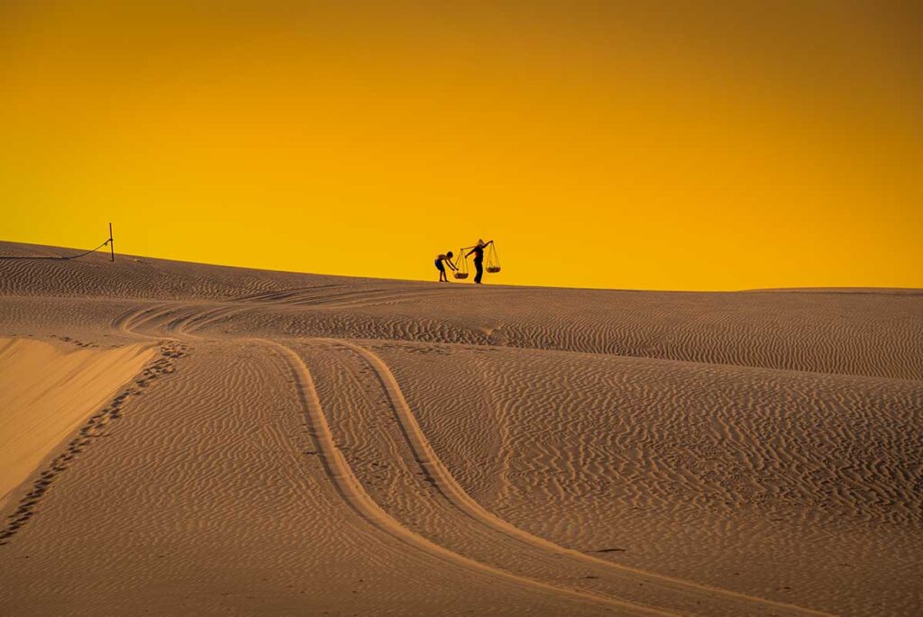 Silhouettes of locals carrying baskets across Nam Cuong Sand Dunes at sunset, Phan Rang
