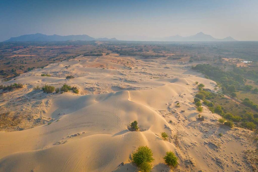 Aerial view of Nam Cuong Sand Dunes near Phan Rang with golden sand hills and distant mountains in Ninh Thuan, Vietnam
