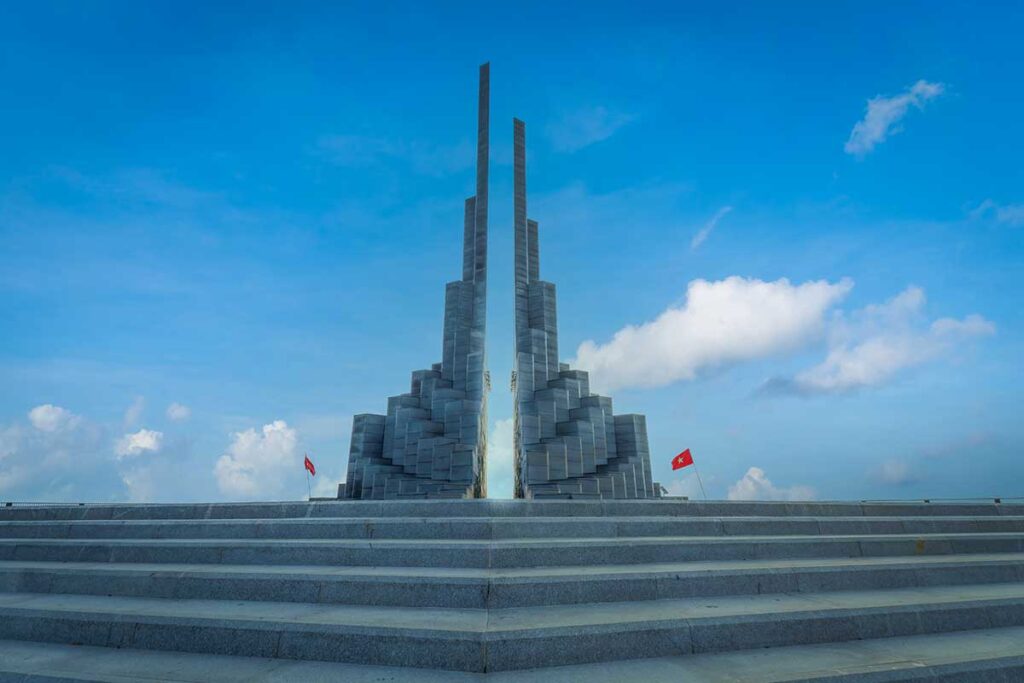 Steps leading up to the twin stone columns of Nghinh Phong Tower with blue sky overhead.