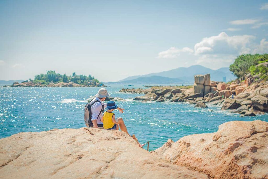 Nha Trang Vietnam – Local Vietnam tours | family sitting on coastal rocks overlooking the blue sea and islands of Nha Trang Bay