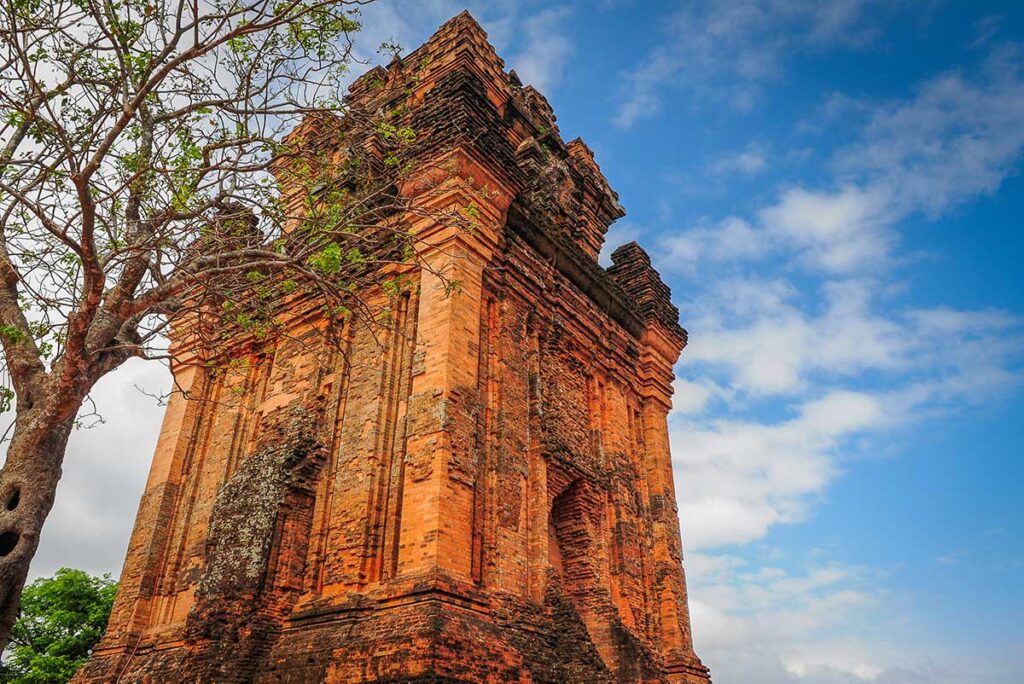 Side angle of Nhan Cham Tower with weathered Cham bricks and tree in the foreground