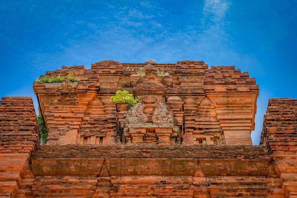 Close-up of decorative carvings on Nhan Tower’s upper brick structure against blue sky