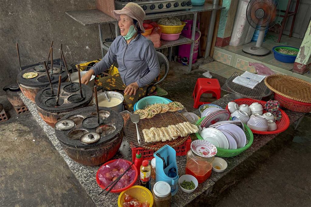 Local woman cooking banh xeo muc – Traditional squid pancakes being prepared on clay stoves, a specialty street food unique to Nhon Hai.