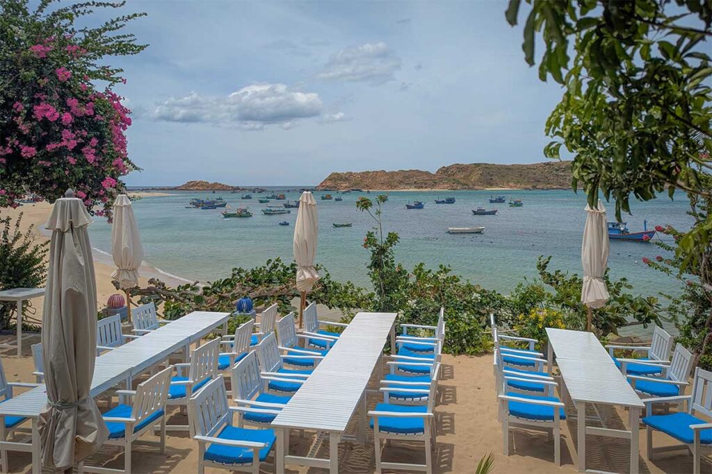 Beachfront dining in Nhon Hai – Outdoor tables with umbrellas overlooking the sea, offering views of fishing boats and the rugged coastline.
